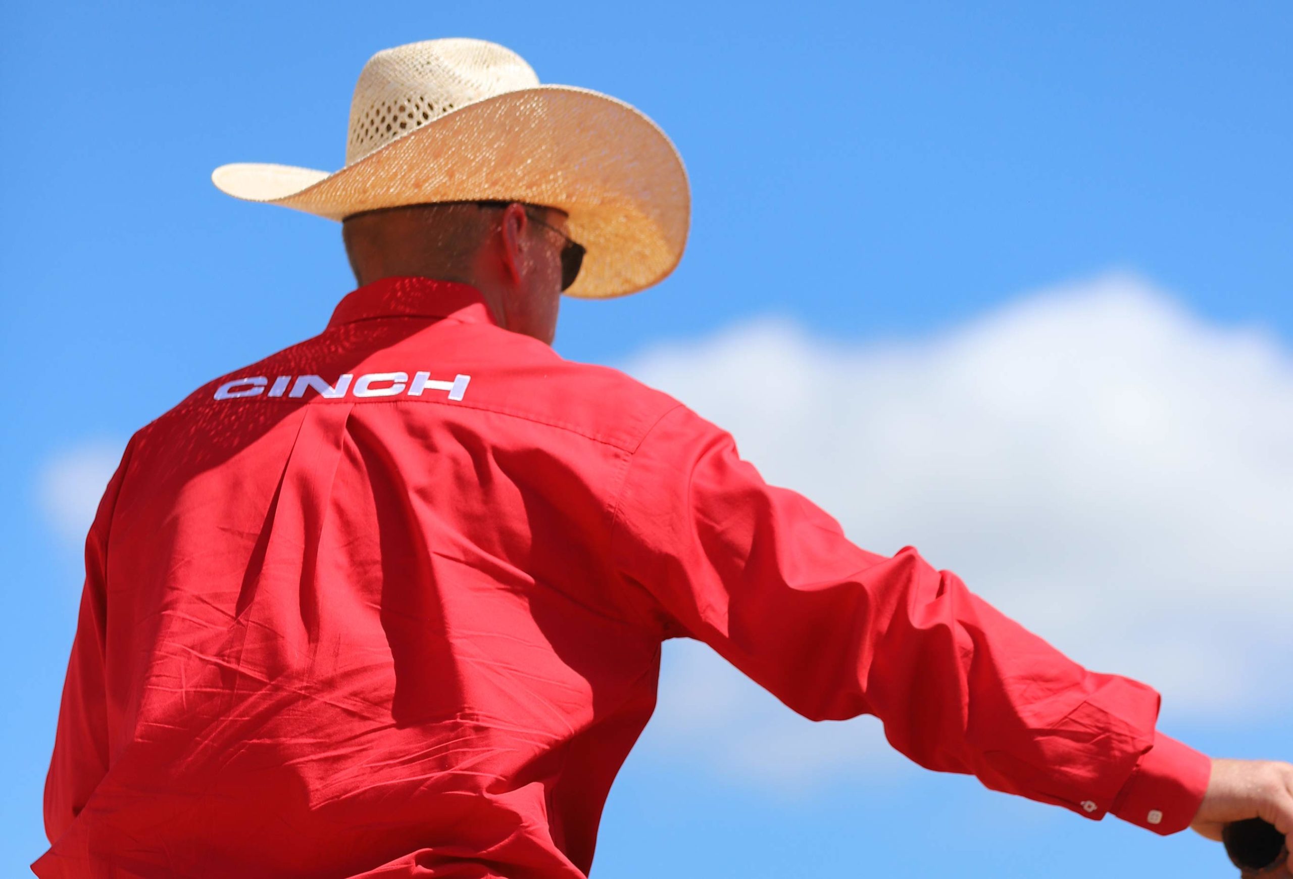Four Sixes Ranch cowboy in a red CINCH shirt and straw hat riding horseback on the Texas plains, representing the ranching traditions, horsemanship, and working cowhorse heritage of the legendary 6666 Ranch.
