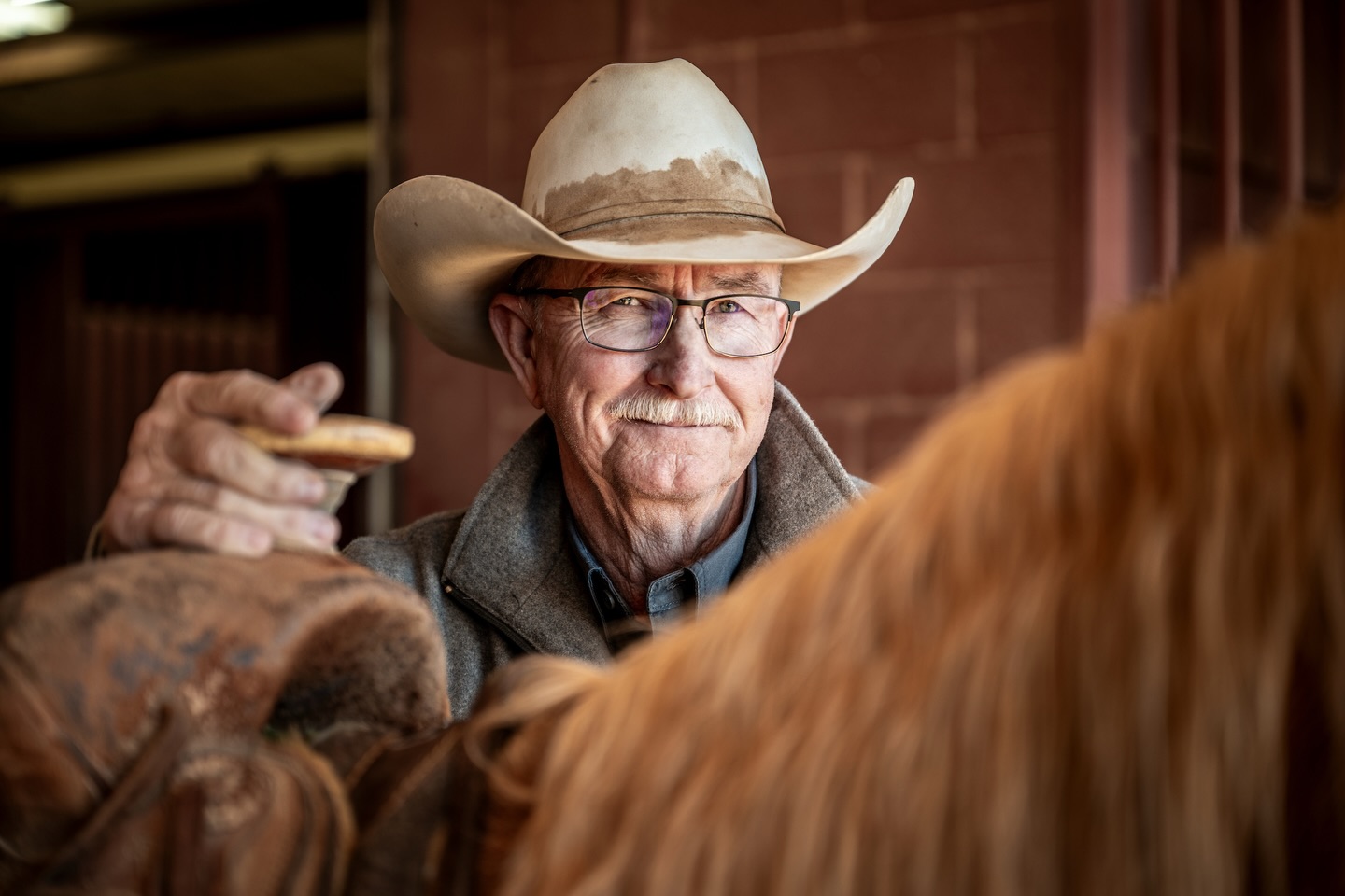 home-staging_01 Joe Leathers holding a saddle horn on a horse, smiling, wearing glasses, and a cowboy hat.